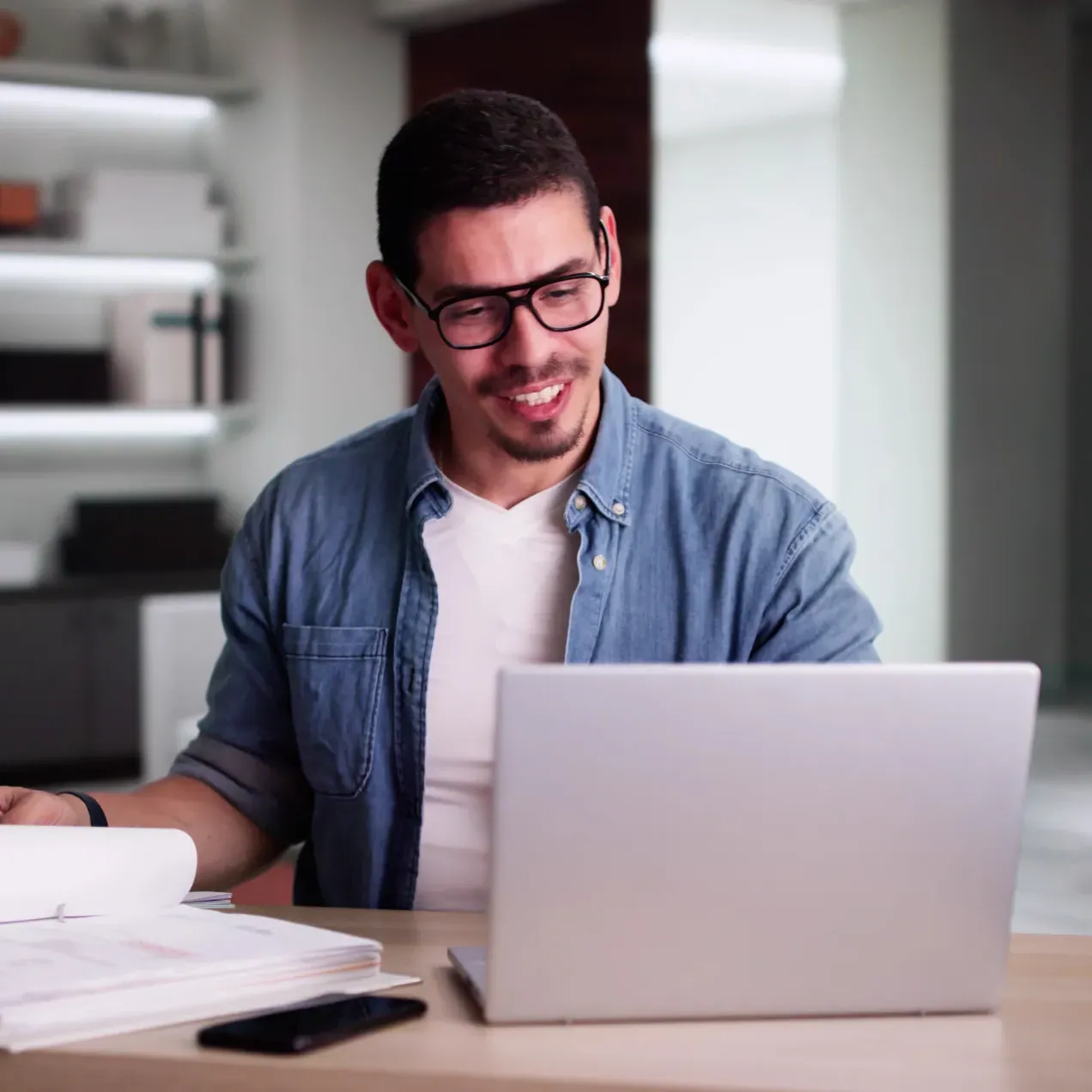 A man in a casual business setting studies financial documents and works on a laptop, representing career opportunities with a Herzing University accounting degree.